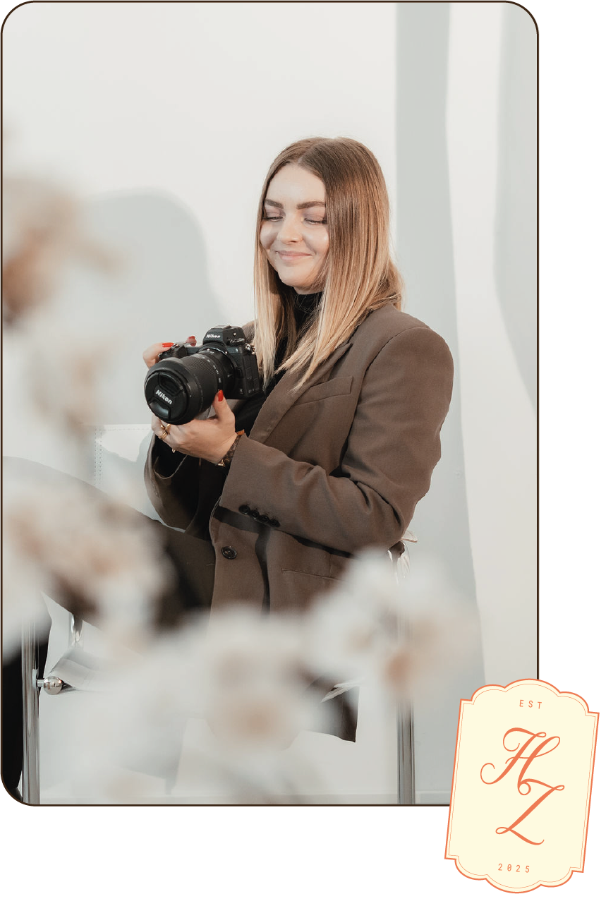 photo@300x ne femme est assise sur un canapé, tenant un appareil photo posé sur ses genoux. Le fond présente un motif à rayures bleues et blanches, apportant une ambiance moderne et épurée. En haut ou en coin de l’image, un logo en forme de sticker avec les lettres « HZ » ajoute une signature visuelle distinctive.